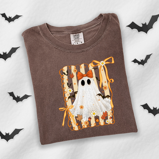 A brown crewneck t-shirt featuring a Halloween graphic of a white ghost with black eyes, an orange bow, and bats, laid flat on a white background with black bat silhouettes.