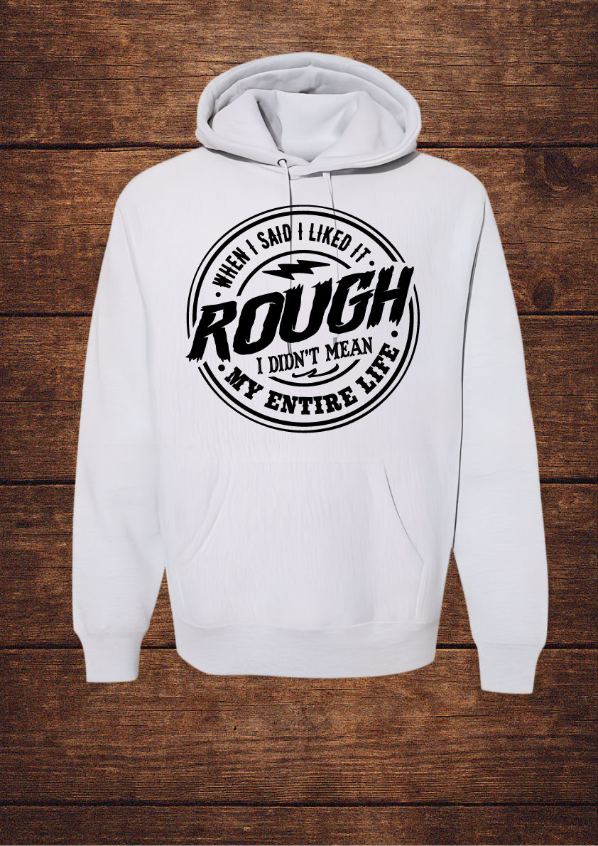 Grey hoodie with black circular design and bold typography stating 'WHEN I SAID I LIKED IT ROUGH I DIDN'T MEAN MY ENTIRE LIFE'; features a drawstring hood and front pouch pocket, laid flat on rustic wood