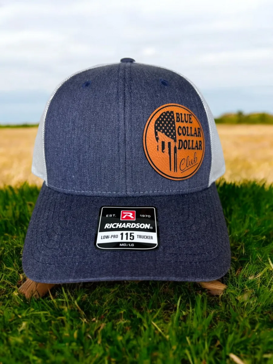 Blue denim cap with orange logo on grass with field and sky in the background