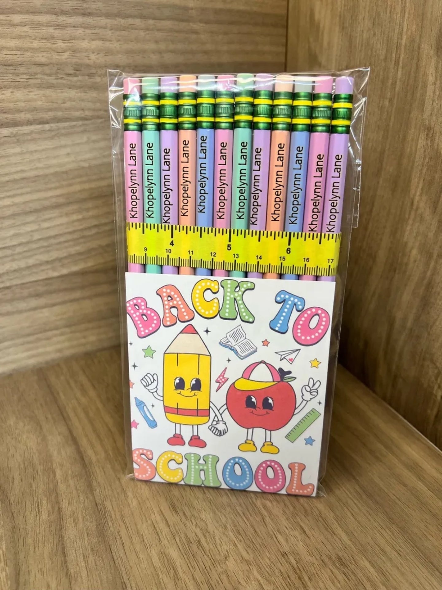 Pack of colored pencils with a 'Back to School' themed card on a wooden surface