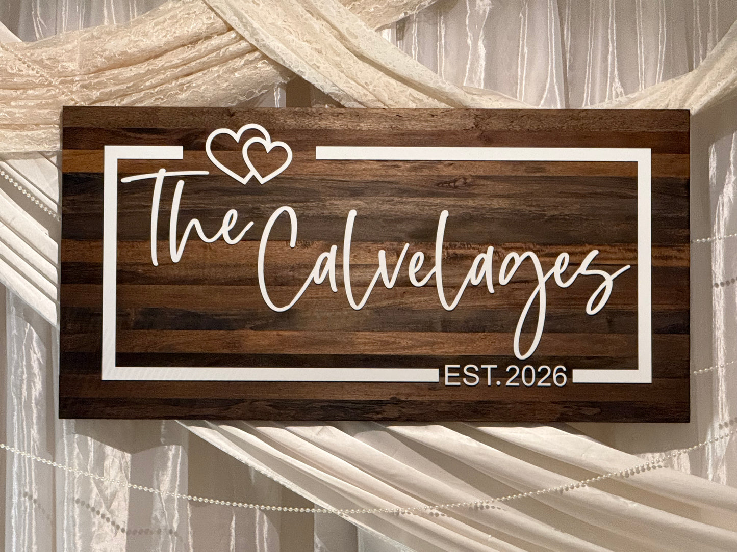 Custom engraved wedding sign with white acrylic name, hearts, and border on dark stained wood. Personalized wedding décor displayed on an easel for ceremony and reception entrance