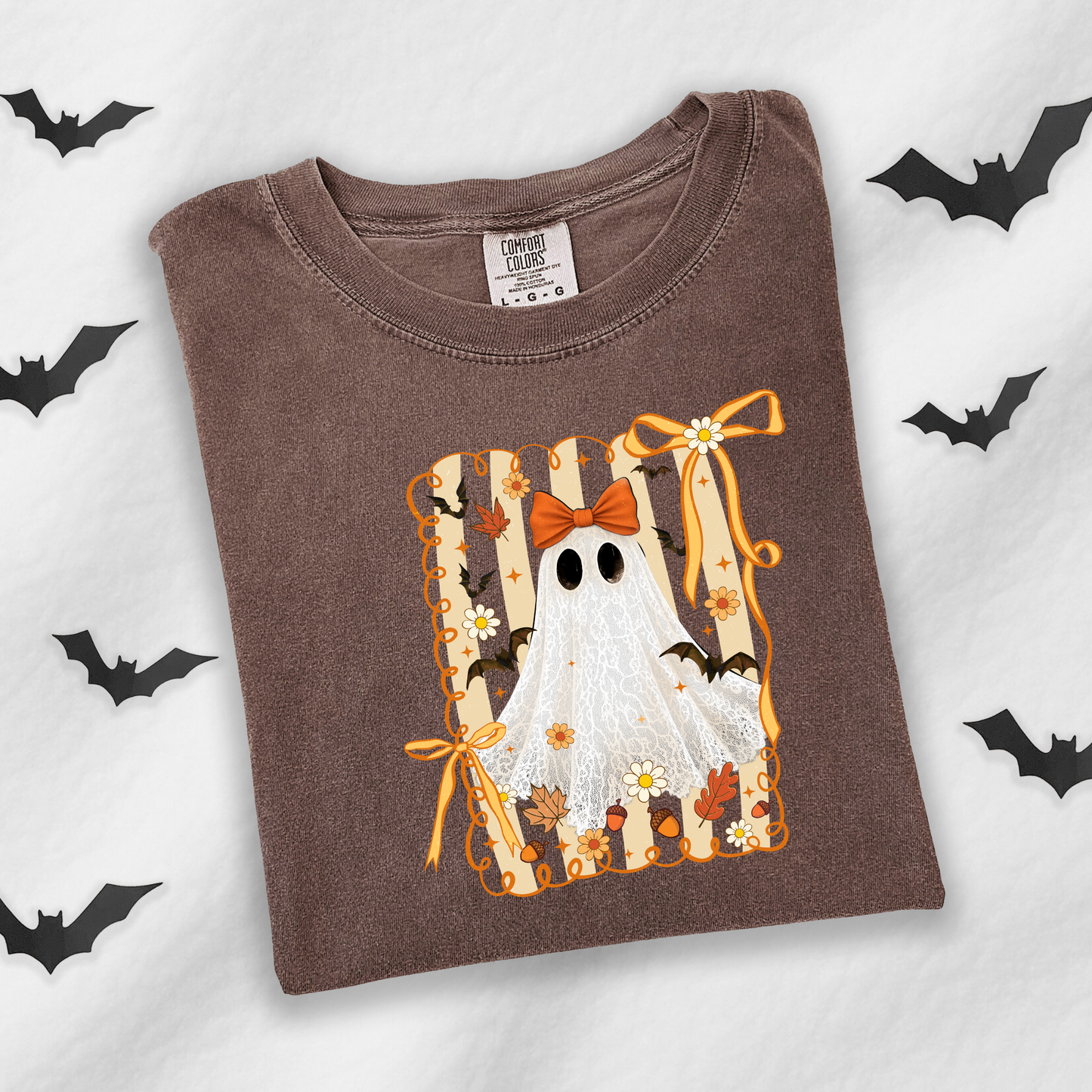 A brown crewneck t-shirt featuring a Halloween graphic of a white ghost with black eyes, an orange bow, and bats, laid flat on a white background with black bat silhouettes.