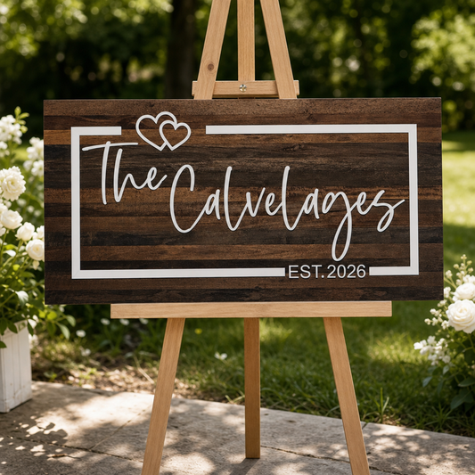 Custom engraved wedding sign with white acrylic name, hearts, and border on dark stained wood. Personalized wedding décor displayed on an easel for ceremony and reception entrance