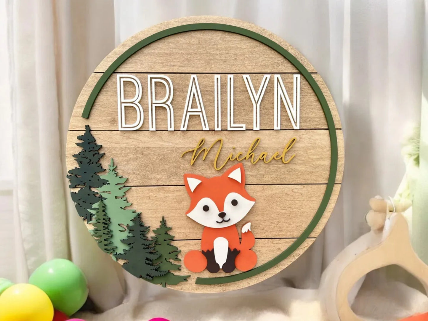 Wooden circular sign with a fox illustration and names 'BRAILYN' and 'Michael' against a white curtain background.