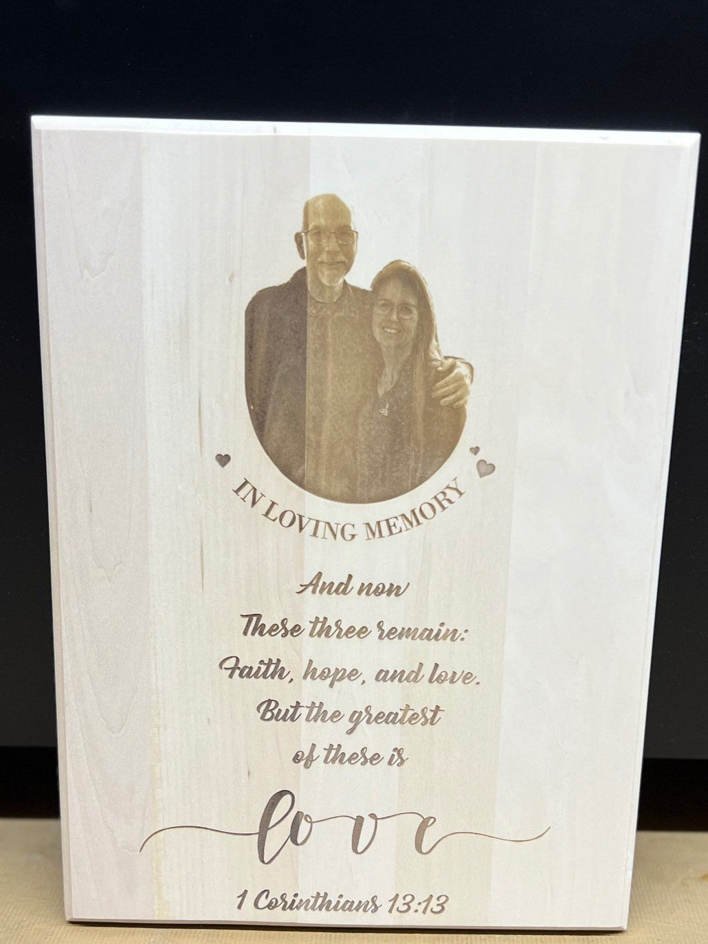 Memorial plaque with a photo of a couple and engraved text on a wooden surface.